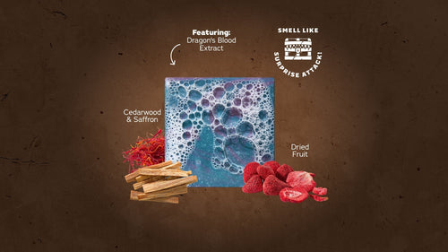 Mimic Bricc bar soap surrounded by ingredients: cedar wood sticks, saffron threads, dried raspberries, and blue textured soap with bubbles on brown background.
